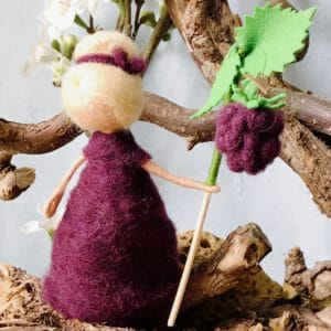 Blumenkind Brombeere aus Filz – tiefes Brombeerviolett, mit gefilzter Brombeere an grünem Stiel. Handgefertigt in Bremen, waldorfinspiriert. Haut- und Haarfarbe anpassbar. Unikat für den Jahreszeitentisch.