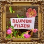 Blumen filzen ist eine wundervolle Möglichkeit in die Welt des nassfilzen einzusteigen. Dieses Bild zeigt eine gefilzte Rose vor einer Vintage Holzwand um ein Schilf auf dem steht: Blumen Filzen. Das Bild umrahmt ein goldener antiker Bilderrahmen mit vielen Schnörkeln. Es wirbt für Onlinekurse zum Blumen filzen